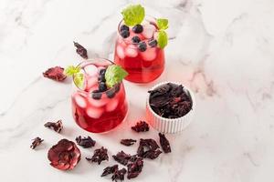 Zwei Glasgläser mit kaltem Hibiskustee, Heidelbeeren, Limettenscheiben und Eiswürfeln auf einem Marmortisch. hoher Gehalt an Vitaminen, Antioxidantien. foto