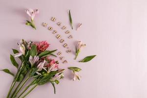eine festliche Komposition zum Muttertag aus wunderschönen Frühlingsblumen und Inschriften in Holzbuchstaben. rosa Hintergrund. Ansicht von oben. foto