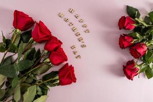 eine festliche komposition aus roten rosen auf rosa hintergrund mit der aufschrift in holzbuchstaben - glücklicher muttertag. Ansicht von oben. flaches Styling. foto