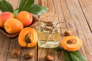 Aprikosenöl in Glasflasche auf dem Hintergrund reifer Aprikosen und Samen. Holzhintergrund. das Konzept der Verjüngung, Befeuchtung der Haut. foto