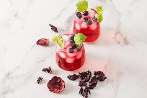 Zwei Glasgläser mit kaltem Hibiskustee, Heidelbeeren, Limettenscheiben und Eiswürfeln auf einem Marmortisch. hoher Gehalt an Vitaminen, Antioxidantien. foto