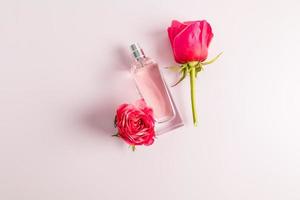 Parfüm in einer Glasflasche auf rosafarbenem Hintergrund mit Knospen frischer Rosen. Ansicht von oben. eine Kopie des Raums. Vorlagenlayout. foto