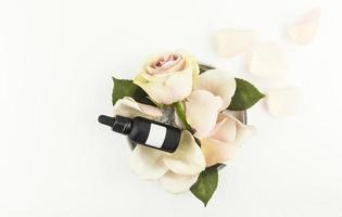 Draufsicht auf eine Schüssel mit Rosenblättern und eine Knospe mit einer Kosmetikflasche aus dunklem mattem Glas mit einem leeren Aufkleber. markenloses Mockup. foto