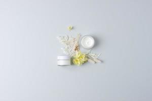 Gläser kosmetische Creme mit Blumen auf grauem Hintergrund. flach liegend, kopierraum foto