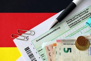 deutsches einkommensteuererklärungsformular mit stift und europäischen euro-geldscheinen liegt auf der flagge in der nähe. steuerzahler in deutschland verwenden euro-währung, um steuern zu zahlen foto