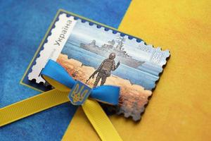 ternopil, ukraine - 2. september 2022 berühmter ukrainischer poststempel mit russischem kriegsschiff und ukrainischem soldaten als hölzernes souvenir auf nationalflagge foto