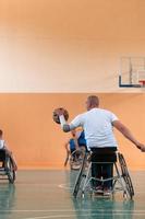 Behinderte Kriegsveteranen gemischte Rassen- und Alters-Basketballteams in Rollstühlen, die ein Trainingsspiel in einer Sporthalle spielen. Rehabilitations- und Inklusionskonzept für behinderte Menschen