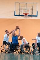 Behinderte Kriegsveteranen gemischte Rassen- und Alters-Basketballteams in Rollstühlen, die ein Trainingsspiel in einer Sporthalle spielen. Rehabilitations- und Inklusionskonzept für behinderte Menschen foto