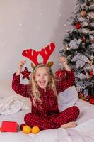 glückliches kleines blondes mädchen zu hause im pyjama für weihnachten, sortieren von geschenken und spielen mit weihnachtsspielzeug foto