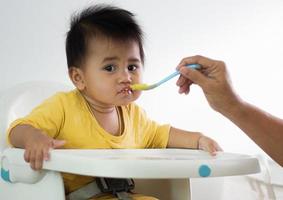 süßes weißes Mädchen sitzender Stuhl beim Frühstück im Innenbereich, der köstliche Mahlzeiten füttert, die sehr nahrhaft sind. Das Baby hat ein fröhliches Gesicht, lustig lächelnd und glücklich in einem gesunden Familienlebensstil. foto