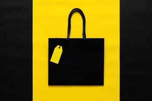 schwarze einkaufstasche mit leerem gelbem preisschild auf gelbem und schwarzem hintergrund für das verkaufskonzept des schwarzen freitags. foto