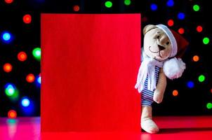 weihnachtsmann-teddybär mit leerer roter karte und buntem bokeh hellem hintergrund. foto