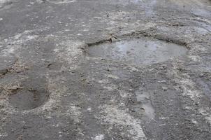 Beschädigte Asphaltstraße mit Schlaglöchern, die durch Frost- und Tauzyklen im Winter verursacht wurden. schlechte Straße foto