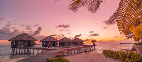 erstaunliches Sonnenuntergangspanorama auf den Malediven. luxus-resort-villen seelandschaft mit palmblättern unter buntem himmel. schöner romantischer himmel und bunte wolken. schöner strandurlaub urlaub, inselparadies foto