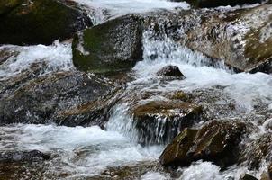 Nahaufnahme eines kleinen wilden Wasserfalls in Form von kurzen Wasserströmen zwischen Bergsteinen foto