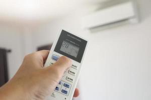 Hand mit Fernbedienung auf die Klimaanlage im Raum gerichtet foto