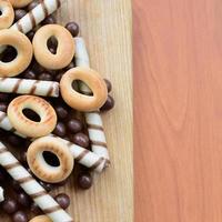 Knusprige Röhrchen, Schokoladenschmelzkugeln und Bagels liegen auf einer Holzoberfläche. Mischung aus verschiedenen Süßigkeiten foto