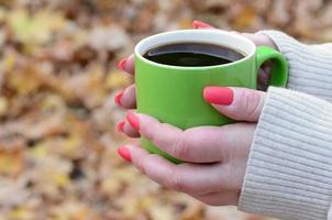 Frau mit weißem Pullover, die eine grüne Kaffeetasse hält foto