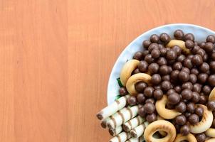 knusprige röhrchen, schokoladenkugeln und bagels liegen in einem weißen teller auf einem holztisch. Mischung aus verschiedenen Süßigkeiten foto