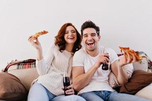 Lachende Frau und Mann, die Pizza essen, während sie sich einen Film ansehen. Innenaufnahme eines glücklichen Paares, das w genießt foto