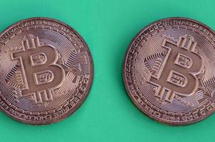 Zwei Schokoladenprodukte in Form von physischen Bitcoins liegen auf einem grünen Kunststoffhintergrund. Modell der Kryptowährung in essbarer Form foto