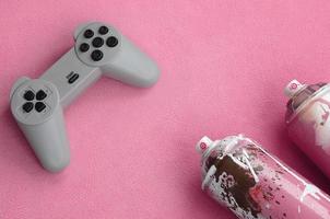 Teenager und Jugend-Lifestyle-Konzept. Joystick und zwei Spraydosen liegt auf der Decke aus flauschigem rosa Fleecestoff. Controller für Videospiele und Farbdosen auf einem Hintergrund aus Plüschvlies foto