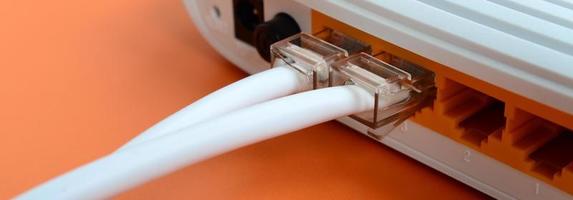 Die Internetkabelstecker sind mit dem Internetrouter verbunden, der auf einem leuchtend orangefarbenen Hintergrund liegt. Elemente, die für die Internetverbindung erforderlich sind foto