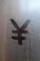 Das chinesische Yen-Symbol wird mit einem Finger auf die Oberfläche des beschlagenen Glases geschrieben foto