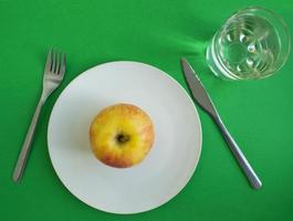 ein Apfel in einem Teller, eine Gabel und ein Messer, ein Glas Wasser foto