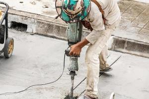 bauarbeiter, der bohrhammer verwendet, der betonoberfläche bohrt foto