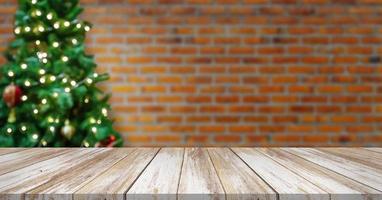 leere hölzerne tischplatte mit unschärfe verziertem weihnachtsbaum mit kugeln auf backsteinmauerhintergrund foto