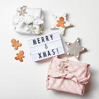 Leuchtkasten Inschrift Frohe Weihnachten, Geschenke im japanischen Furoshiki-Stil und Lebkuchenplätzchen foto