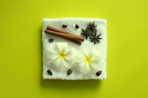 weißes handtuch mit blumen von plumeria mit sternen von anis und zimtstangen auf dem gelben hintergrund für spa-thema. foto