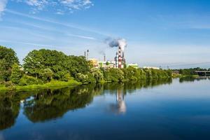 Rohre des Sägewerks des Holzbearbeitungsunternehmens mit schöner Spiegelung im blauen Wasser des Flusses. Luftverschmutzungskonzept. Industrielandschaft Umweltverschmutzung Abfall von Wärmekraftwerken foto