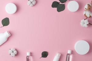 kosmetischer hintergrund mit hautpflegeprodukten und blumen auf rosa. flach liegend, kopierraum foto