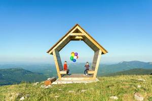 Mädchen und ein Junge sitzen in einem Holzhaus auf einem Berg und halten Luftballons. konzept von sicherheit, versicherung und glänzender zukunft foto