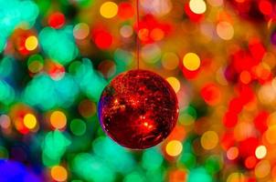 rote kugel, die hängt, um für weihnachtsfeiertage mit buntem bokeh von licht und anderen kugeln zu dekorieren. foto