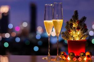 zwei gläser sekt mit weihnachtsbaum- und kugelverzierungen auf tisch mit buntem stadt-bokeh-lichthintergrund. foto