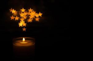 aromatische kerze mit flamme und sternform bokeh auf dunklem hintergrund für danksagung und weihnachtstag. foto
