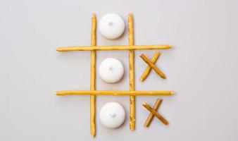 kreatives Modell des Tic-Tac-Toe-Spiels aus Crackern und Keksen auf grauem Hintergrund. Food-Konzept. Essbare Snacks trocknen Sticks mit Salz und Keksen auf einem weißen Teller. Strohhalme, Cracker-Sticks. foto