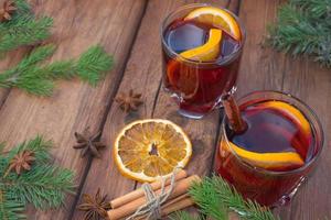 weihnachtsglühwein auf einem hölzernen hintergrund mit gewürzen und fichtenzweigen und getrockneter orange. foto