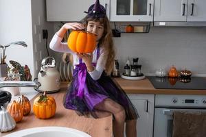 Kind schmückt die Küche zu Hause für Halloween. Mädchen in einem Hexenkostüm spielt mit dem Dekor für den Urlaub - Fledermäuse, Jack-Laterne, Kürbisse. Herbstkomfort im Haus, Küche im Scandi-Stil, Dachboden foto