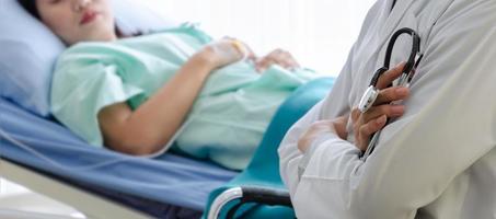 Arzt hält Stethoskop und sitzt vor krankem Patientenbett im Krankenzimmer foto