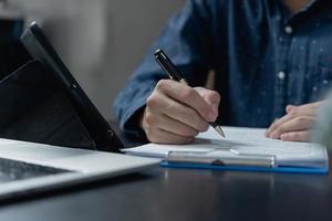 Hand mit Stift schreiben Papierkram Geschäftsdokument Finanzinvestition oder Unterschrift Vertrag Job und Versicherung auf dem Schreibtisch.
