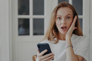 frau ist ein aufgeregtes telefon. rothaarige europäische dame bekommt schock, freiberuflerin hat termin. foto