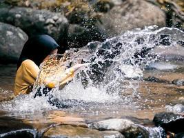 Ein Mädchen im Hijab lässt Wasser im Regenwaldbach spritzen foto