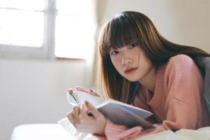 Porträt junge asiatische nette Frau jugendlich College-Student, der am Morgen ein Buch im Schlafzimmer liest.