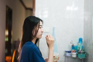 junge erwachsene asiatische frau, die zähne im badezimmer putzt foto