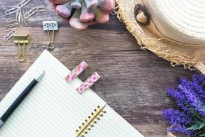 Die flache Lage des femininen Vintage-Sommerkonzepts mit einem offenen rosa Spiralnotizbuch, einem Strandhut, Holzclips und dekorativen Blumen. foto