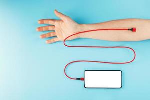 ein smartphone mit einem großen weißen bildschirm ist über ein rotes usb-kabel mit einer vene in der hand auf blauem hintergrund verbunden. foto